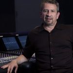 Man sitting in front of large soundboard and monitors